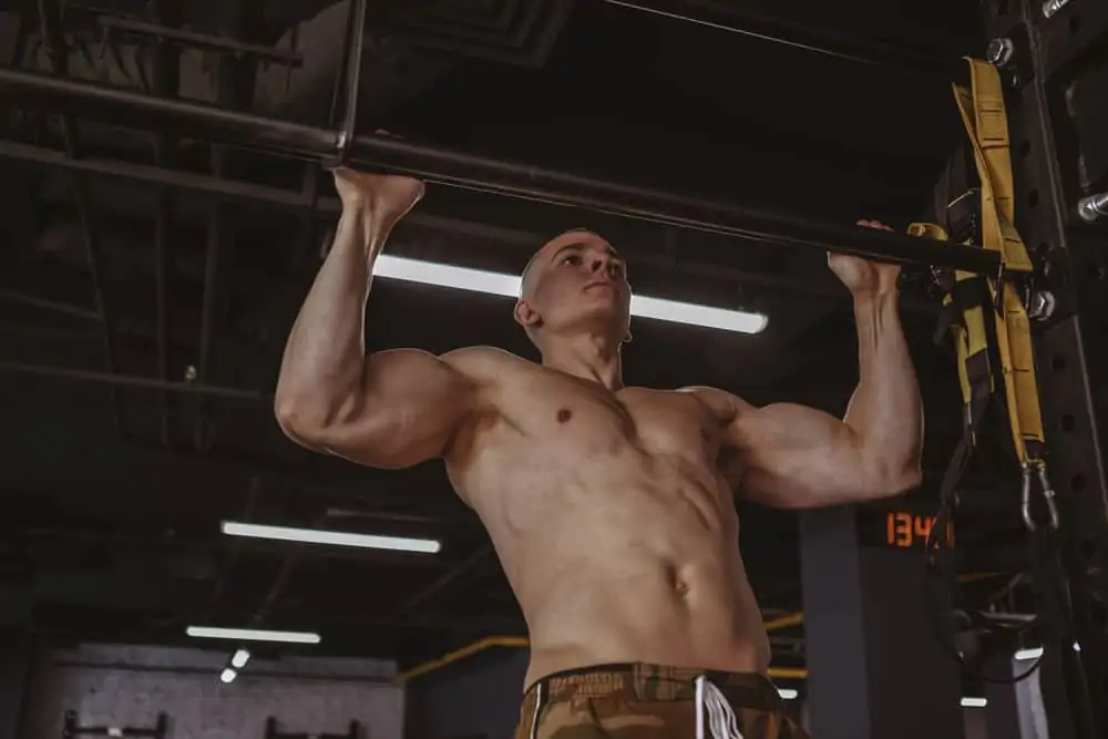 Athletic guy doing pull-up in cross gym